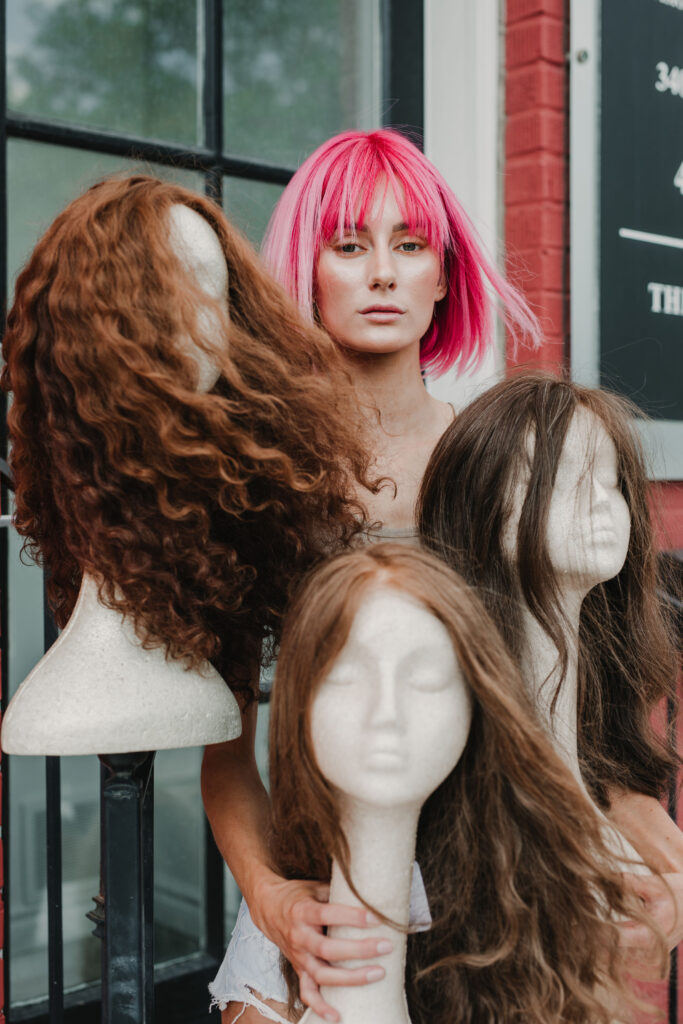 Women with pink wig holding up multiple wig styles