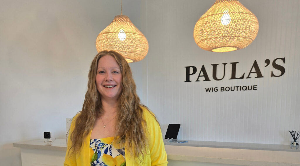 Woman in curly blonde natural wig standing in Paula's boutique wig store